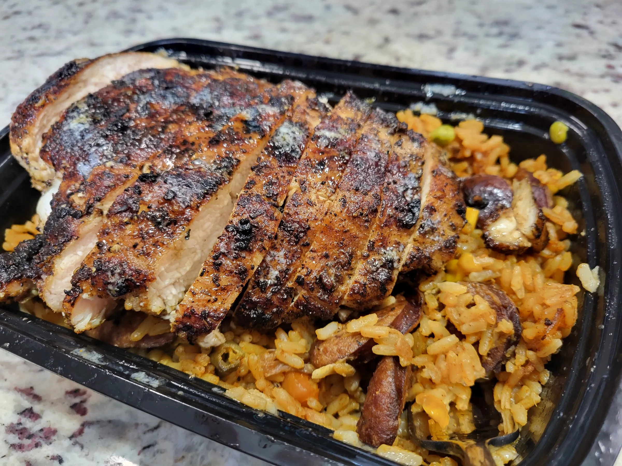 Meal prep tray of sliced chicken over yellow rice with mushrooms and corn